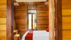 Ein Zimmer in einer Holzhütte mit einem Bett, einem kleinen Tisch und einem Fenster mit Gitterwerk.