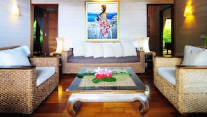 Un rincón de descanso acogedor con muebles de mimbre, una mesa baja con un centro de flores y un cuadro grande sobre el sofá.