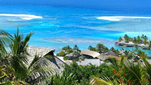 Un resort costero con bungalows sobre el agua, palmeras y aguas azules cristalinas.