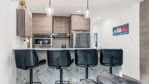 Een moderne keuken met een backsplash in een herringbone-patroon, roestvrijstalen apparatuur en een bar voorzien van vier zwarte barkrukken.