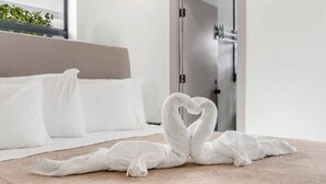 Een hotelkamer met een bed, een handdoekarrangement in de vorm van een hart op de vloer, en een deur op de achtergrond.