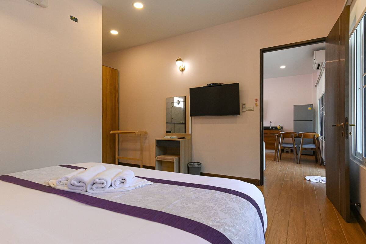 A hotel room with a bed, a desk, a chair, a television, and a bathroom visible through an open door.