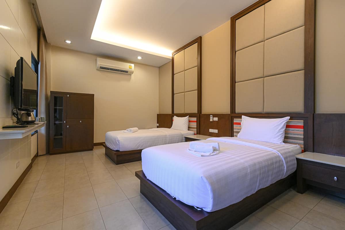 A hotel room with two single beds, a wooden wardrobe, a small desk, and a television.