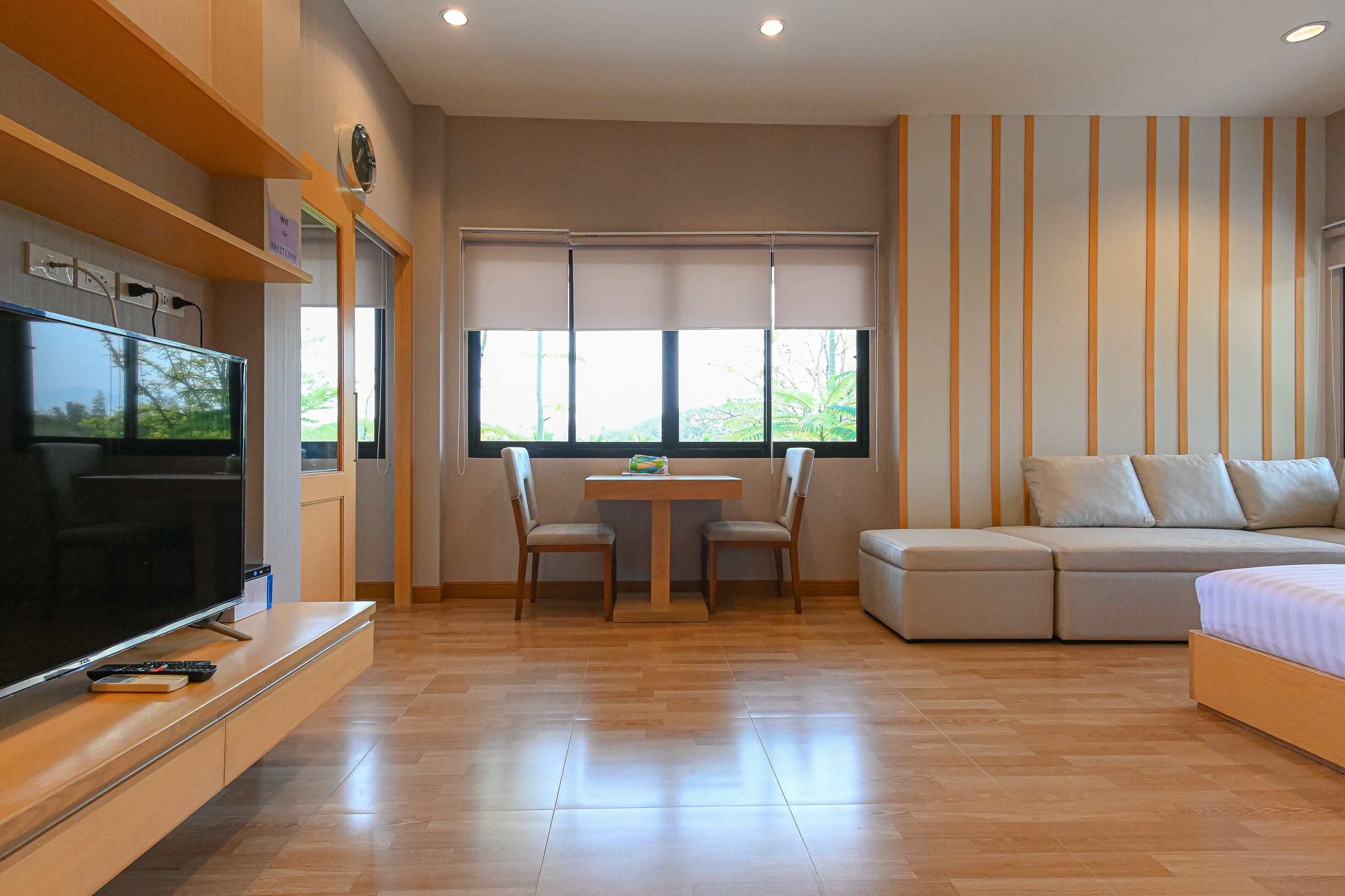 Una sala de estar moderna con un televisor de pantalla plana, una mesa de comedor con sillas, un sofá y un ventanal con persianas.