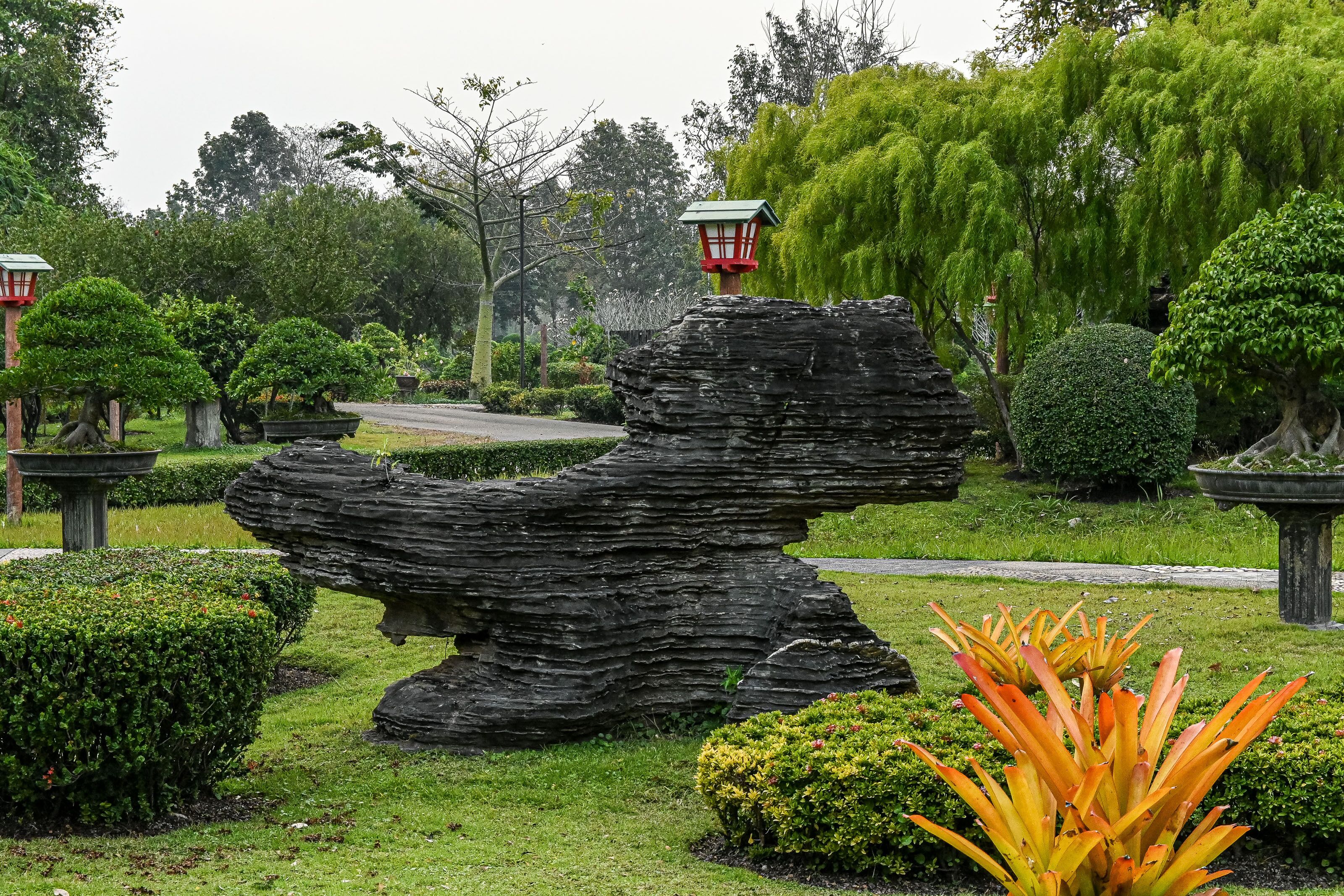 A garden with a large rock formation, a pathway, and various plants.