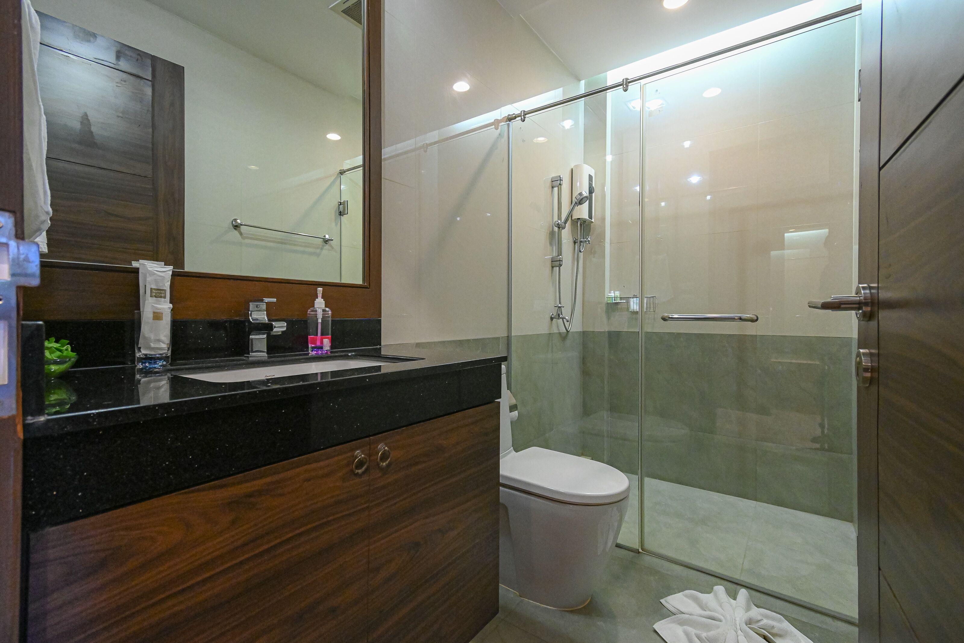 Un baño moderno con ducha de vidrio, tocador de madera con lavamanos y un inodoro.