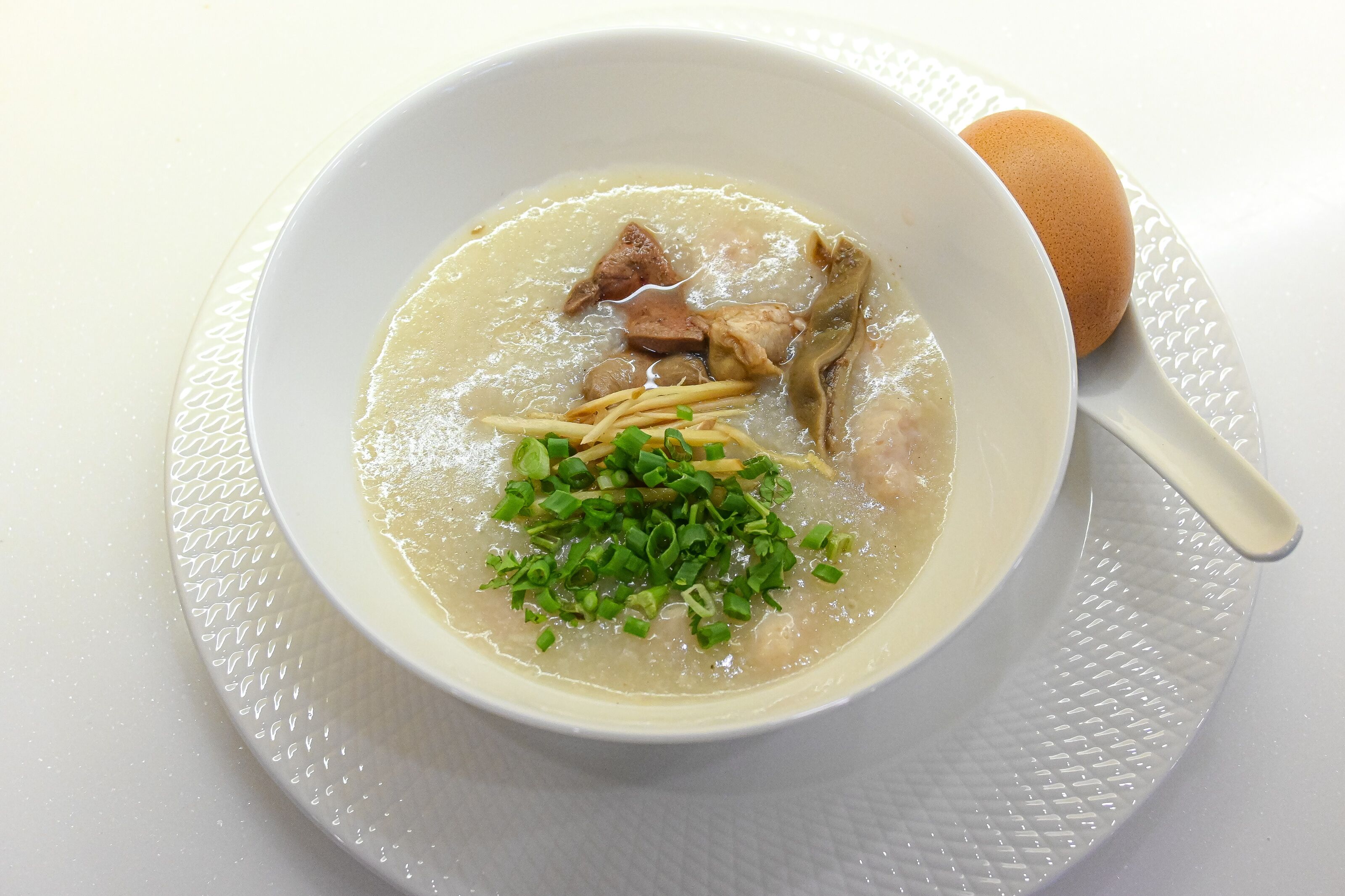A bowl of soup with noodles, meat, and green onions on a white plate.