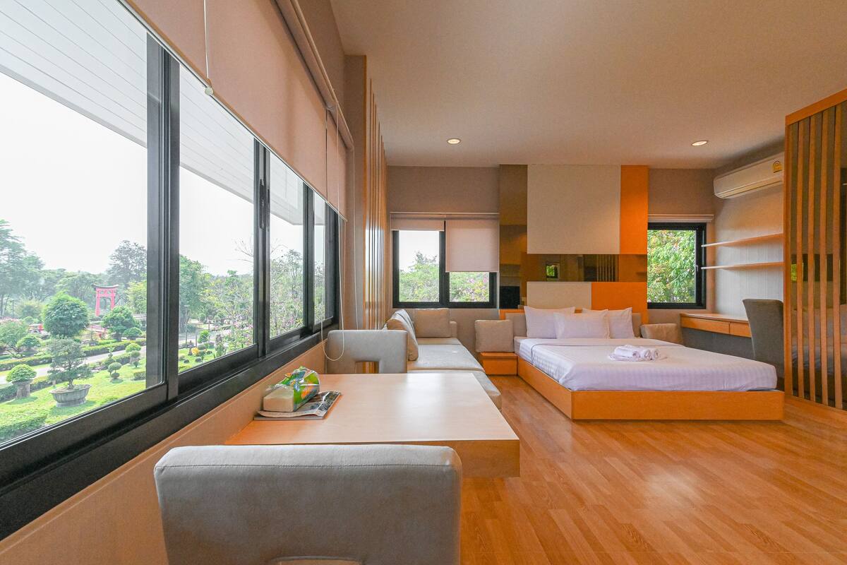 A modern hotel room with a large window, a bed, a desk, and a seating area.