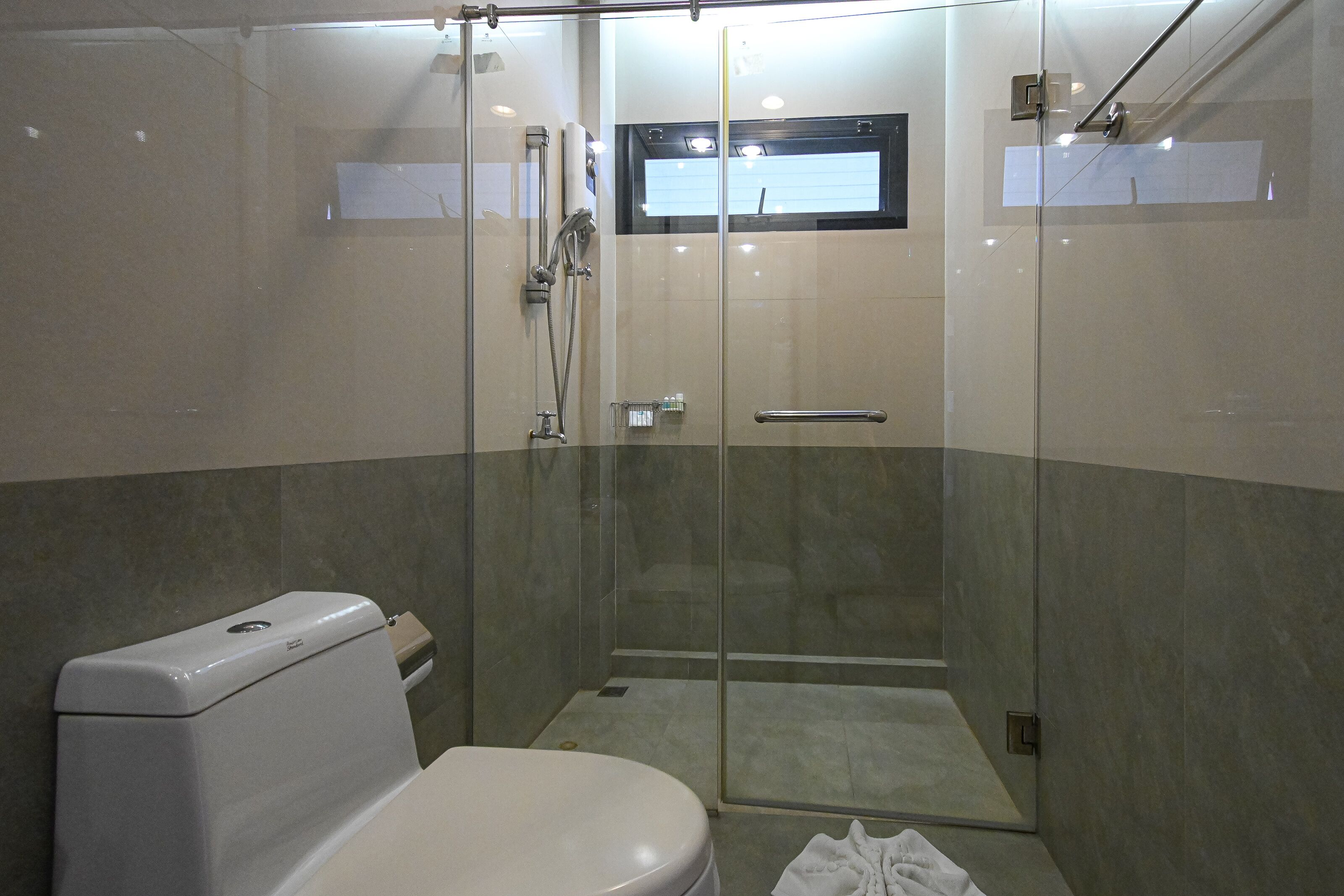 A modern bathroom with a glass-enclosed shower, a toilet, and a small window above the shower.