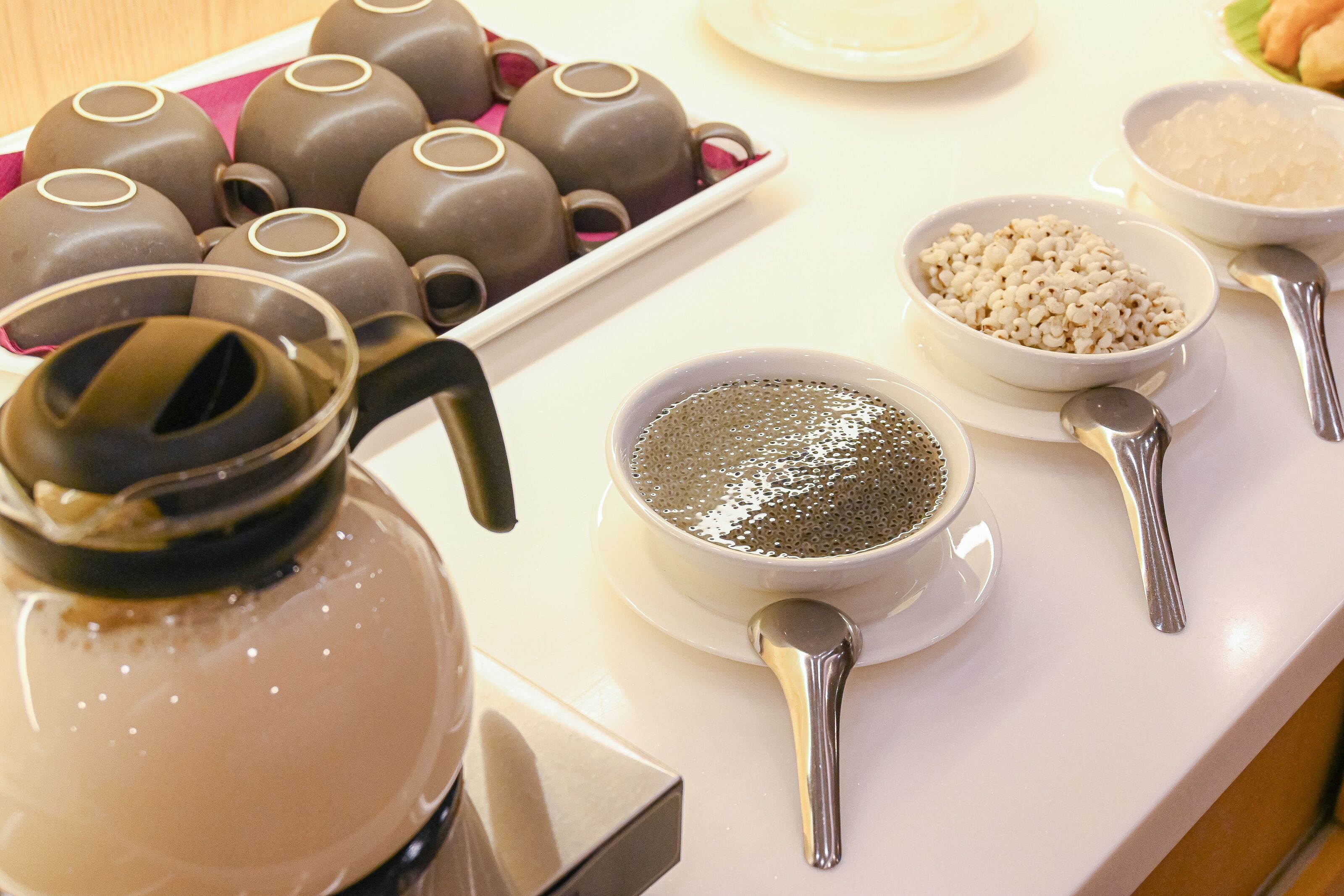 A table with a teapot, teacups, and bowls of rice and other items.