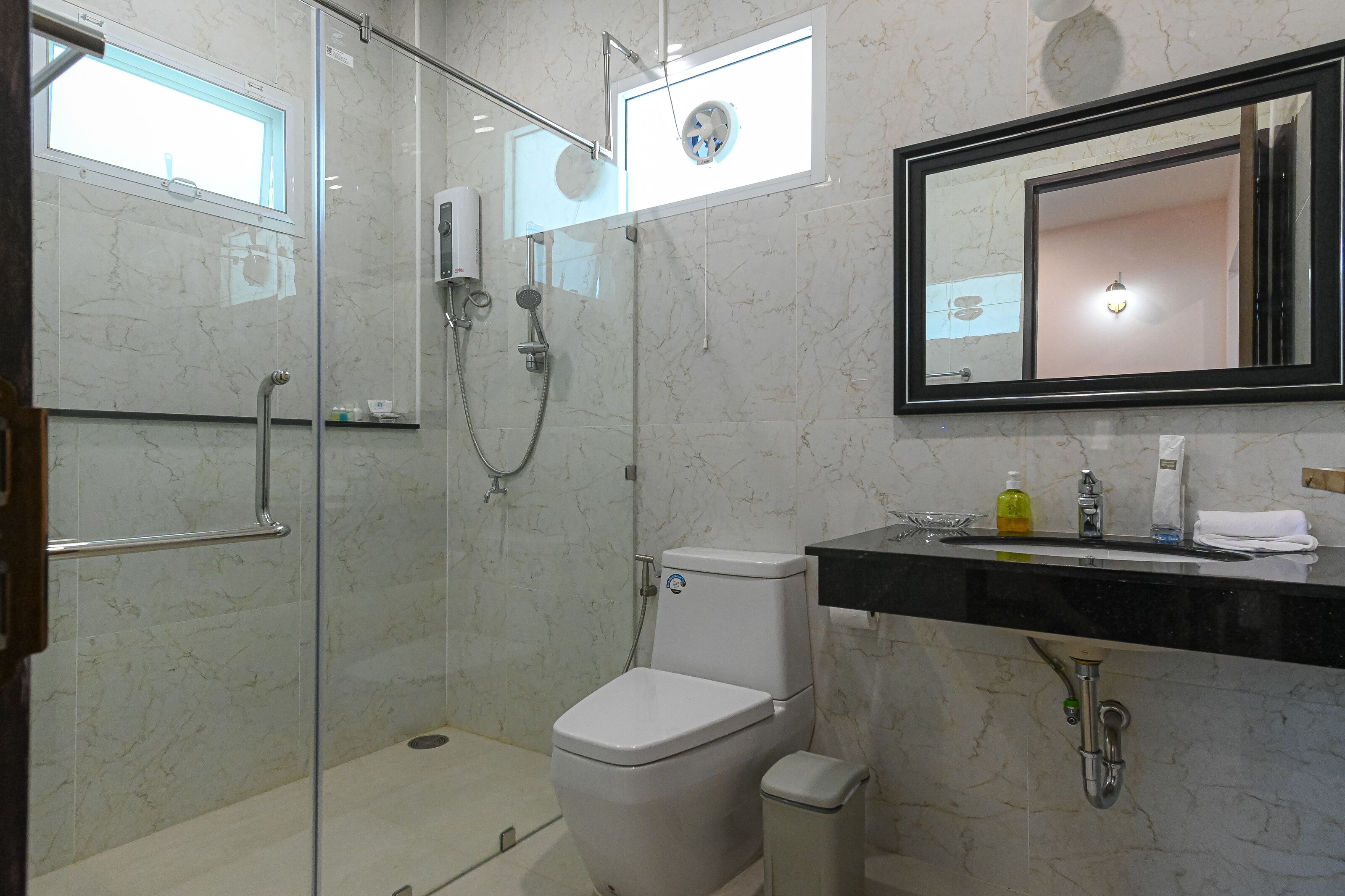 Un bagno con doccia vetro, wc, lavandino con specchio e finestra.