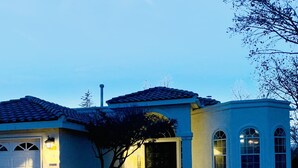 Una casa de dos pisos con techo de tejas, un garaje y una pequeña estructura adosada con ventanas de arco.