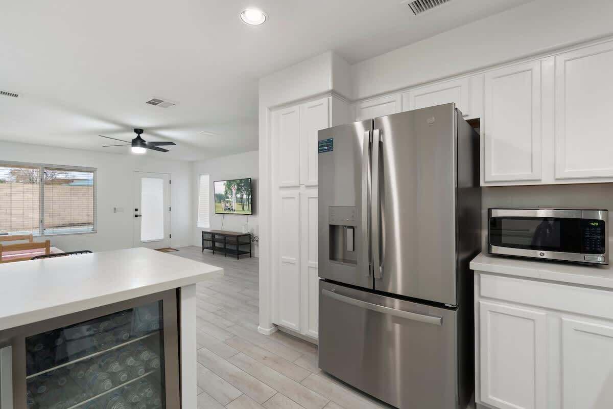 Una cocina moderna con armarios blancos, un refrigerador de acero inoxidable, un microondas y un ventilador de techo.