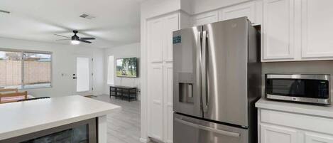 Una cocina moderna con armarios blancos, un refrigerador de acero inoxidable, un microondas y un ventilador de techo.