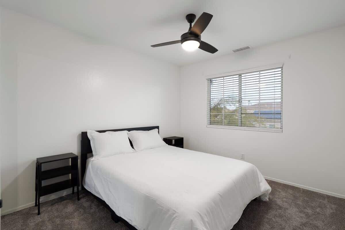 A bedroom with a single bed, a ceiling fan, a nightstand, and a window with blinds.