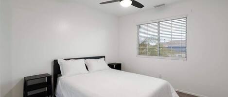 A bedroom with a single bed, a ceiling fan, a nightstand, and a window with blinds.