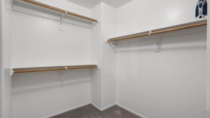 Una esquina de una habitación con paredes blancas y alfombra gris. Se observan tres estantes de madera fijos en las paredes, cada uno con un soporte metálico.