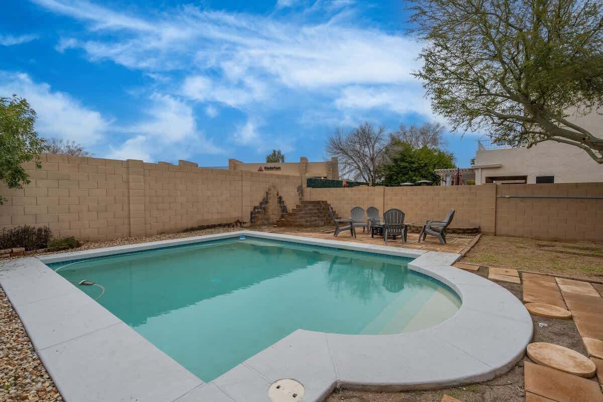 A swimming pool with a built-in hot tub, surrounded by a brick wall and a patio area with outdoor furniture.