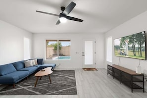 Un salon moderne avec un canapé bleu, une table basse, un téléviseur fixé au mur et un ventilateur de plafond.