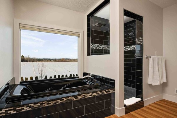 Une salle de bain avec un lavabo aux carreaux noirs, une fenêtre donnant sur un champ et une serviette blanche accrochée au mur.