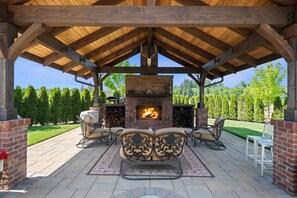 Une terrasse extérieure dotée d’une cheminée en briques, d’un plafond en bois et d’un espace salon.