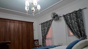 Ein Schlafzimmer mit einem Holzkasten, einem Bett mit weißer Bettwäsche, einer blauen Decke und einem Deckenventilator.