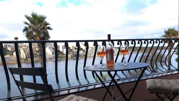 Ein Balkon mit Tisch, zwei Stühlen und einer Weinflasche.