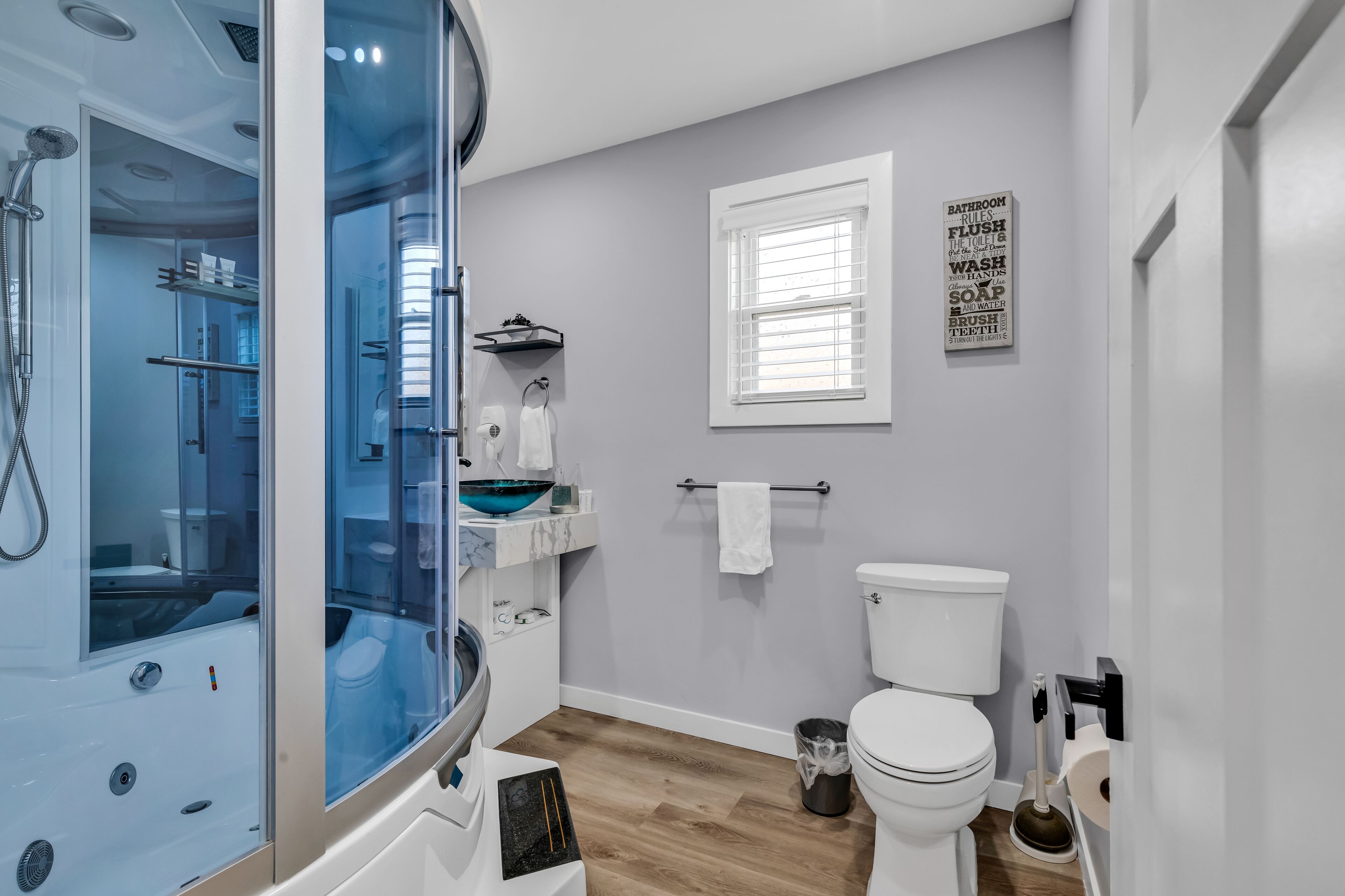 A modern bathroom with a glass-enclosed shower, a white toilet, and a sink with a blue basin.