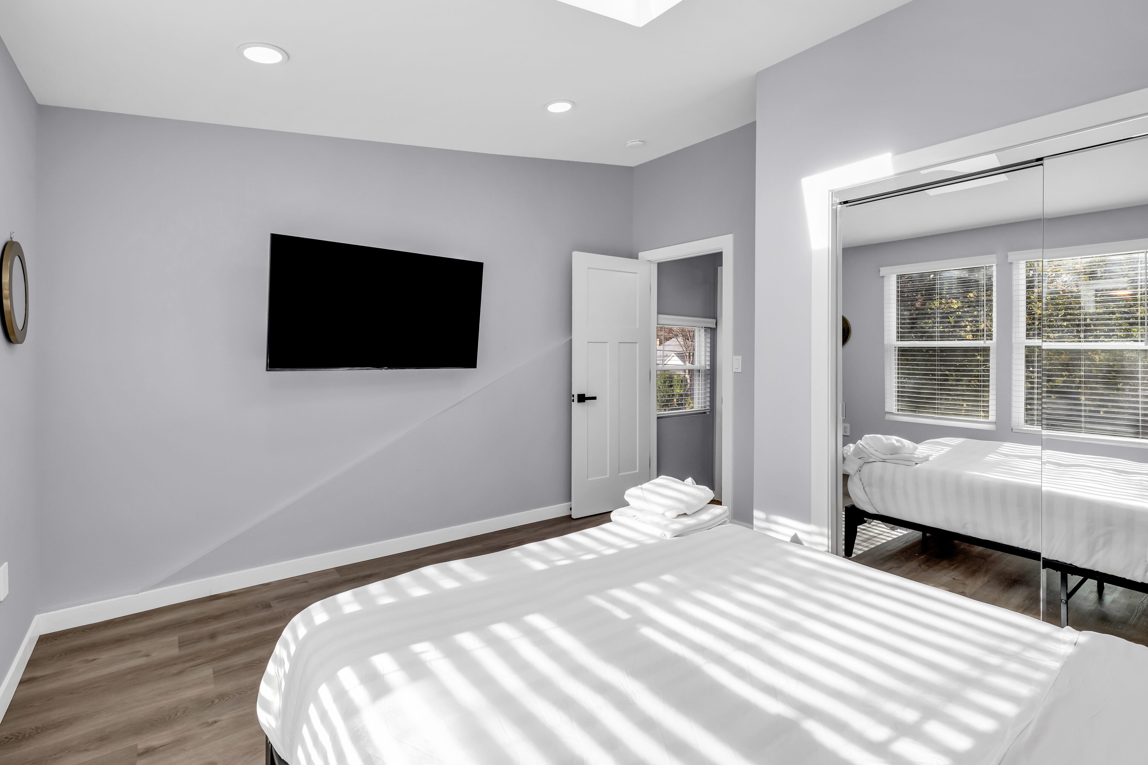 A bedroom with a bed, a TV mounted on the wall, and a window with blinds.