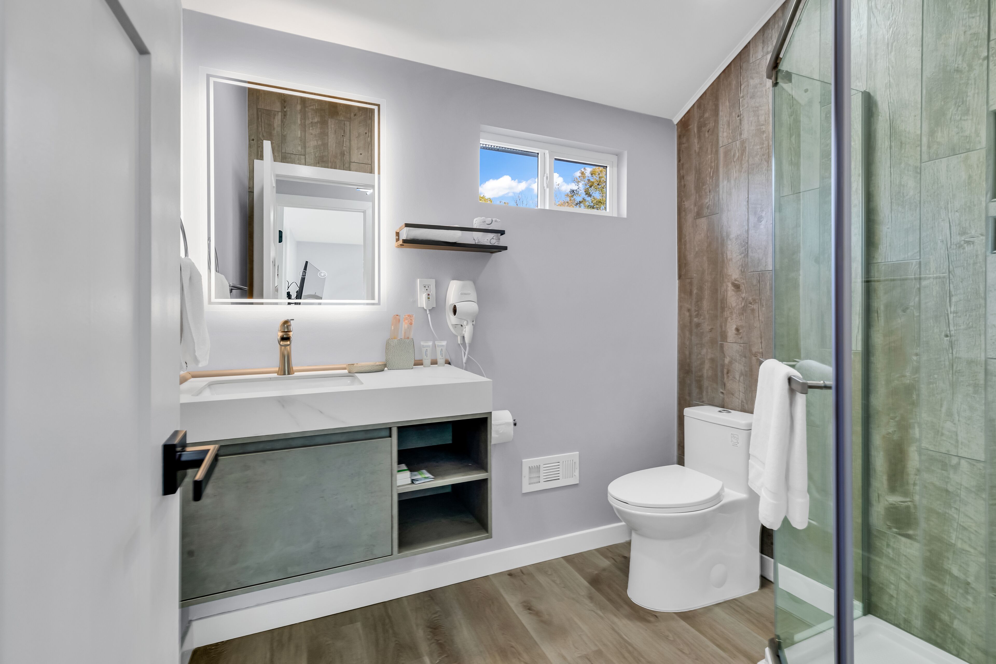 A modern bathroom with a large mirror, a toilet, a shower with glass doors, and a small window.