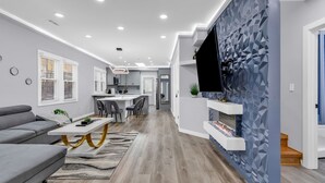 A modern living room with a grey sofa, a white coffee table, and a TV mounted on a geometric-patterned wall. - Spacious 3BR House in Charlotte (Charlotte)
