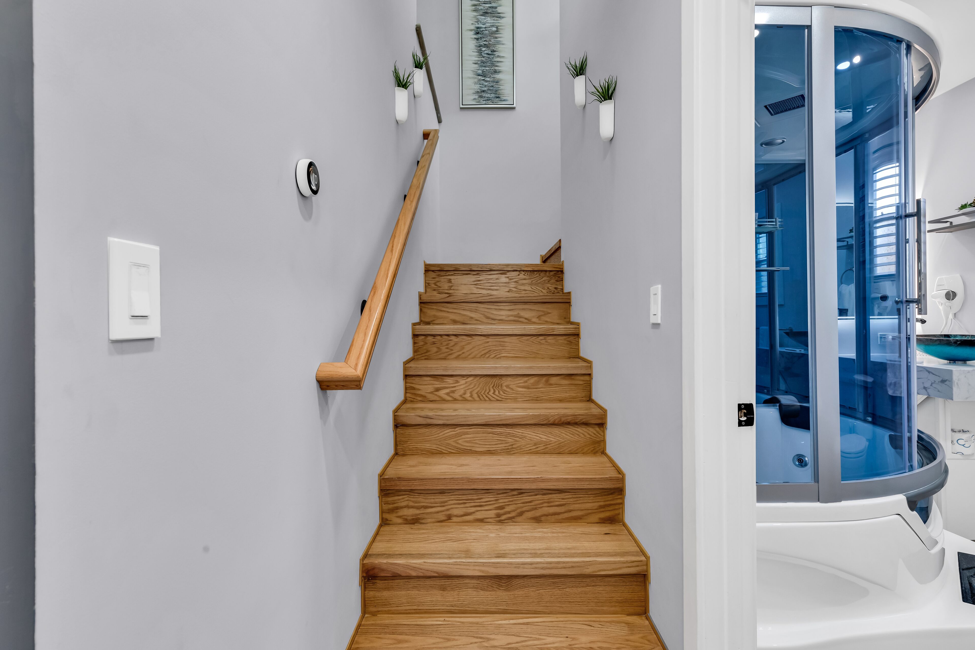 A wooden staircase with a handrail, a light switch, and a framed picture on the wall.