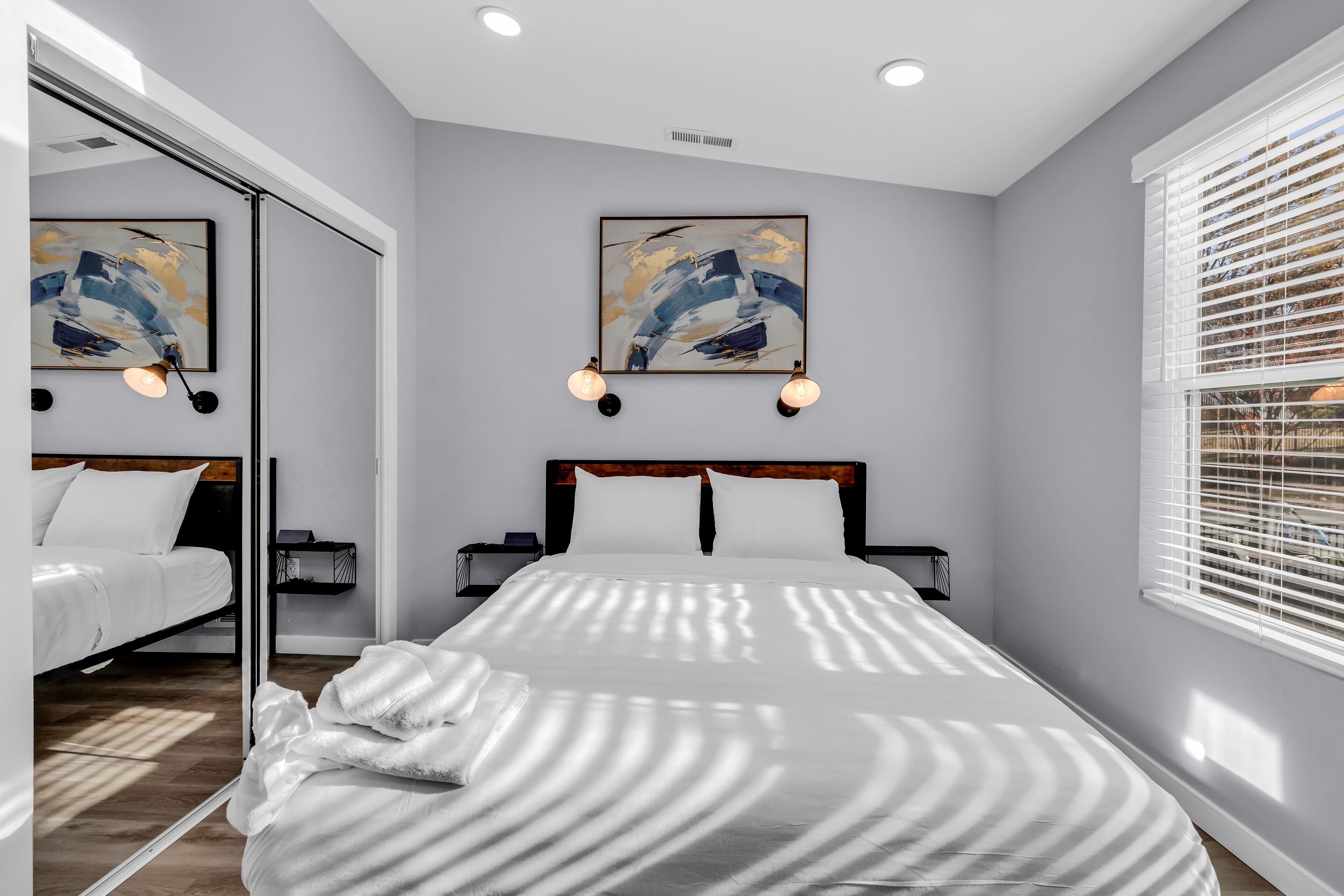 Une chambre moderne avec un grand lit, deux tables de chevet et des œuvres d’art accrochées aux murs.