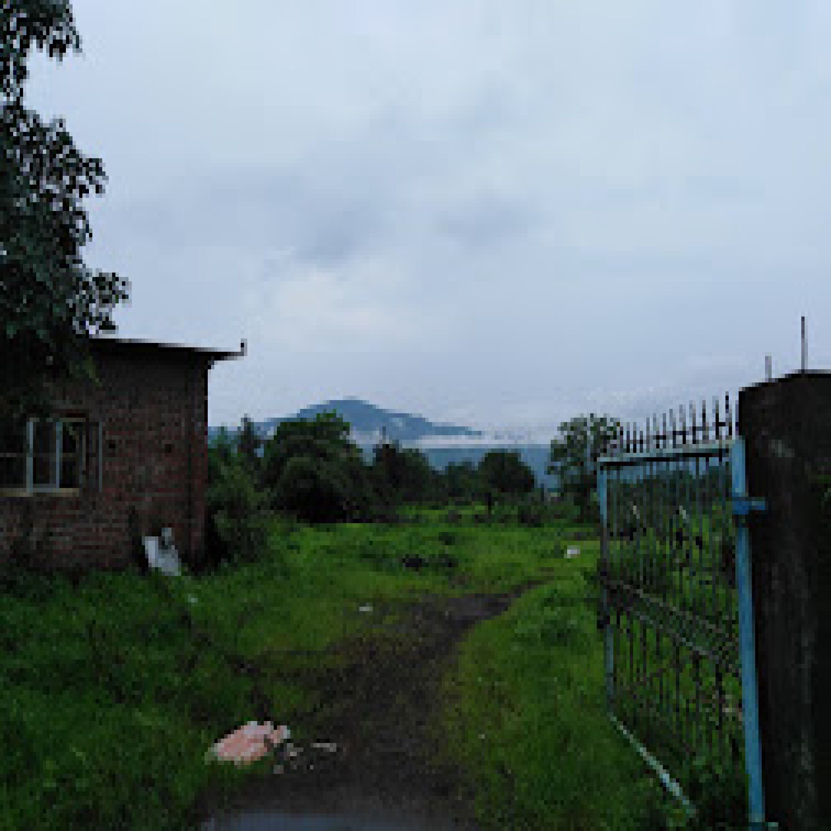 A rural setting with a brick building, a metal gate, and a path leading to a body of water.