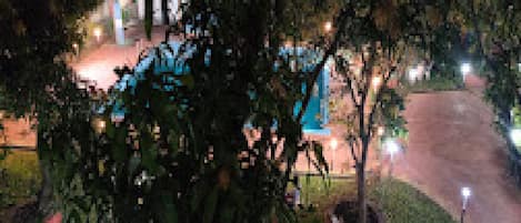 Vista nocturna de un hotel con una entrada bien iluminada y plantas en macetas al frente.