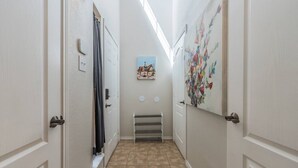 Un couloir étroit avec des portes blanches, un radiateur et une œuvre d’art accrochée au mur.