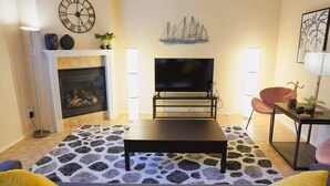 Un salon avec une cheminée, un téléviseur, une table basse et un tapis à motifs.
