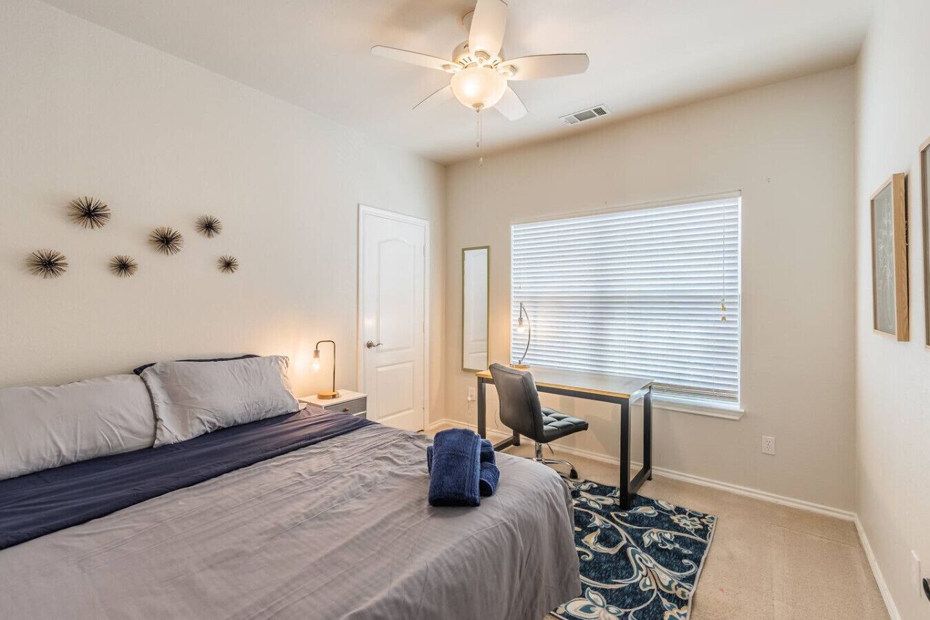 A bedroom with a bed, desk, chair, and a ceiling fan.