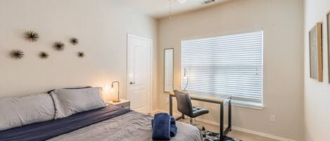 A bedroom with a bed, desk, chair, and a ceiling fan.