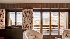A cozy room with a large window, a checkered armchair, a wooden table, and a view of mountains. - Appartement LaForet 86 - La Tzoumaz, 4 Vallees (La Tzoumaz)