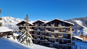 A multi-story hotel with a snow-covered exterior, set against a mountainous backdrop. - Appartement LaForet 86 - La Tzoumaz, 4 Vallees (La Tzoumaz)