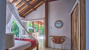 A bedroom with a bed, a bedside table, a mirror, and a view of the outside. - Villa Ketenangan (Ubud)