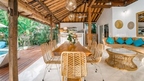 A spacious patio with a wooden deck, a dining table surrounded by wicker chairs, and a glass coffee table. - Villa Ketenangan (Ubud)