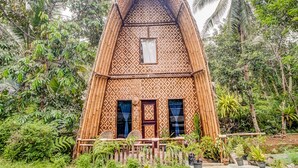 Una casa tradicional de bambú con techo triangular, dos ventanas y un pequeño balcón.