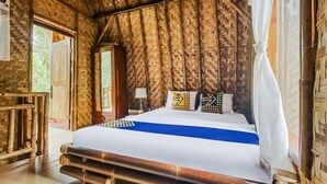 Una habitación con cama, mesita de noche, lámpara y vistas al exterior con vegetación.