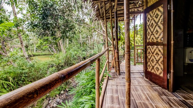 Un puente de madera con barandilla de bambú que conduce a un edificio con una puerta decorada.