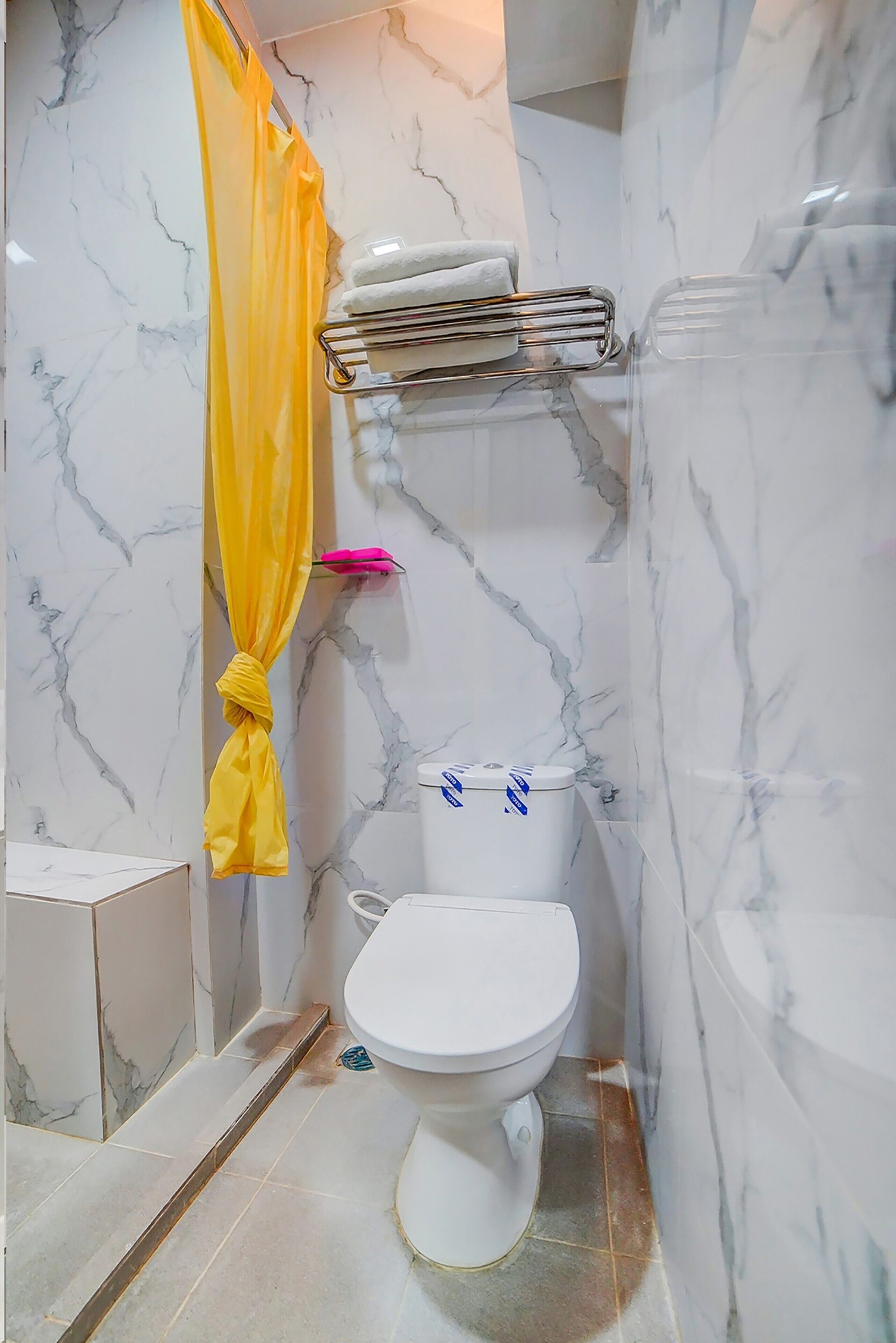 Une salle de bain avec des toilettes blanches, un rideau de douche jaune et des murs en marbre.