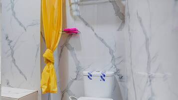 Une salle de bain avec des toilettes blanches, un rideau de douche jaune et des murs en marbre.