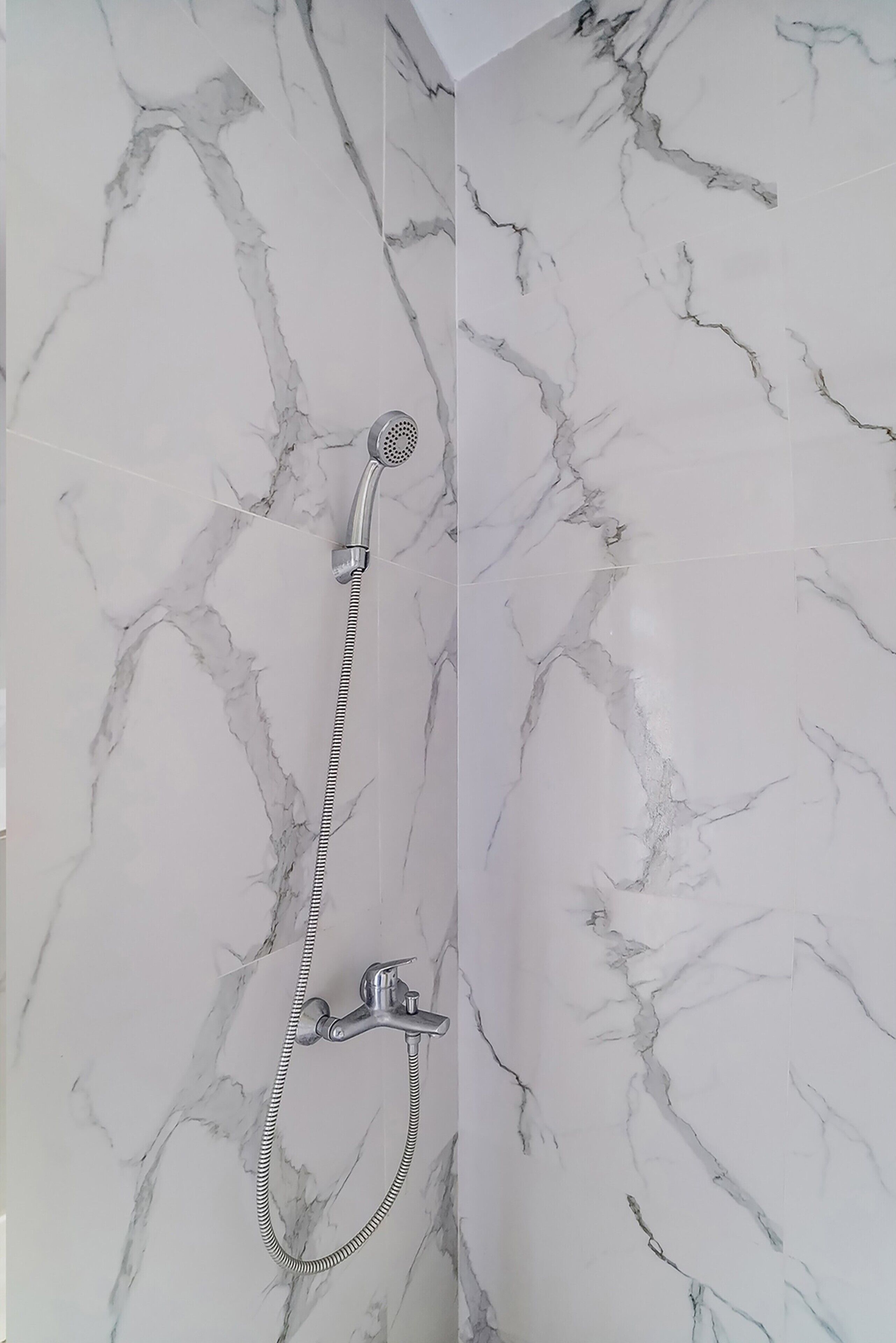 A bathroom with a marble shower wall and a handheld showerhead.