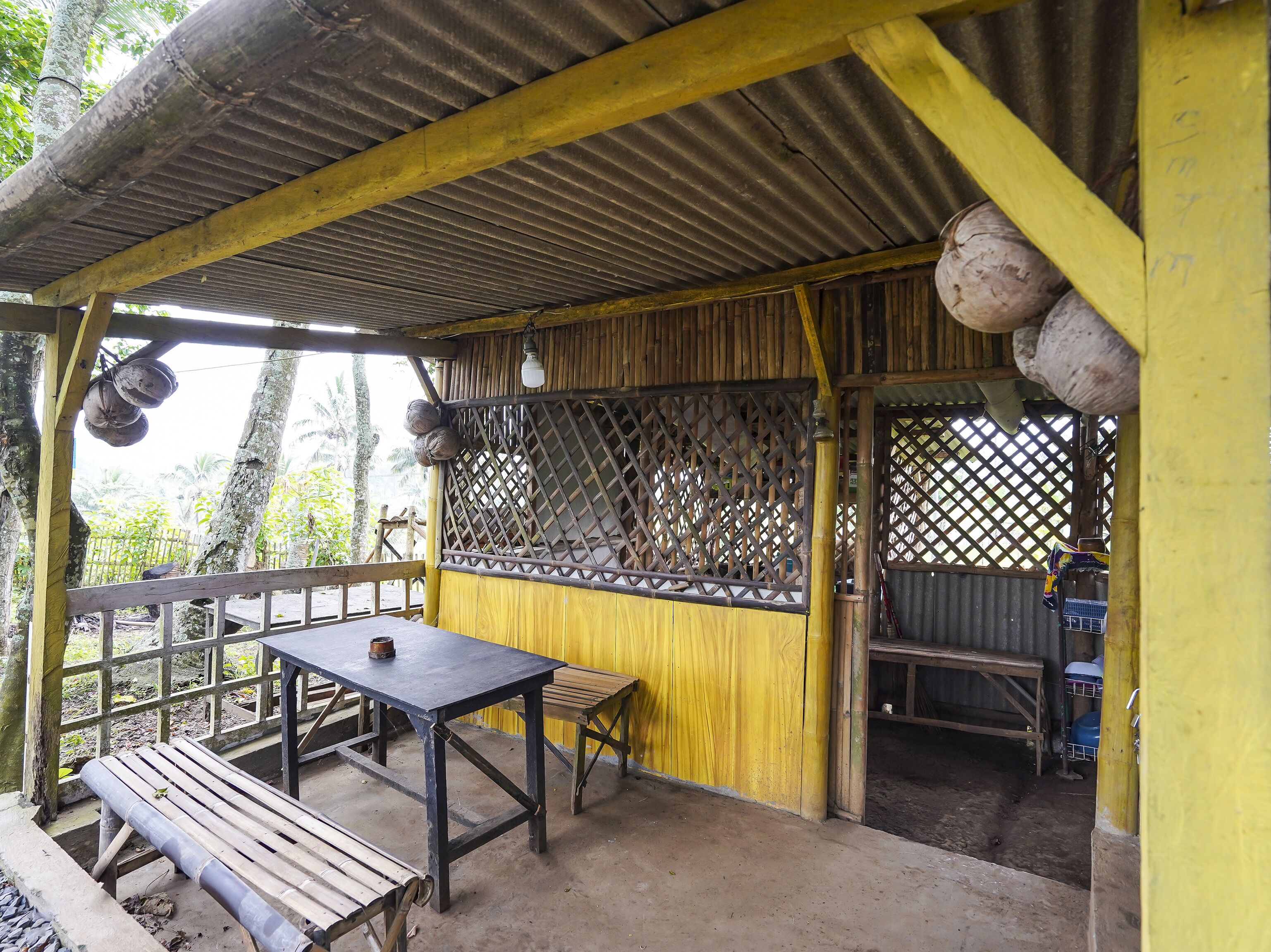 A covered outdoor seating area with a table and benches, surrounded by a wooden fence and a lattice screen.